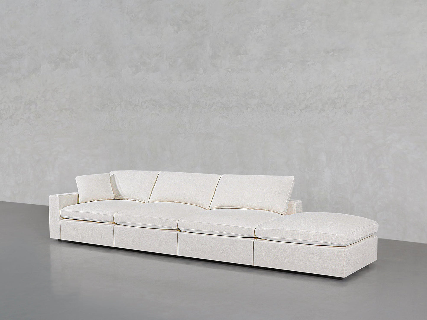 The 4-Seat Modular Lounger Sofa, modern and white with four seat cushions and three back cushions, sits on a smooth grey floor against a light grey textured wall.