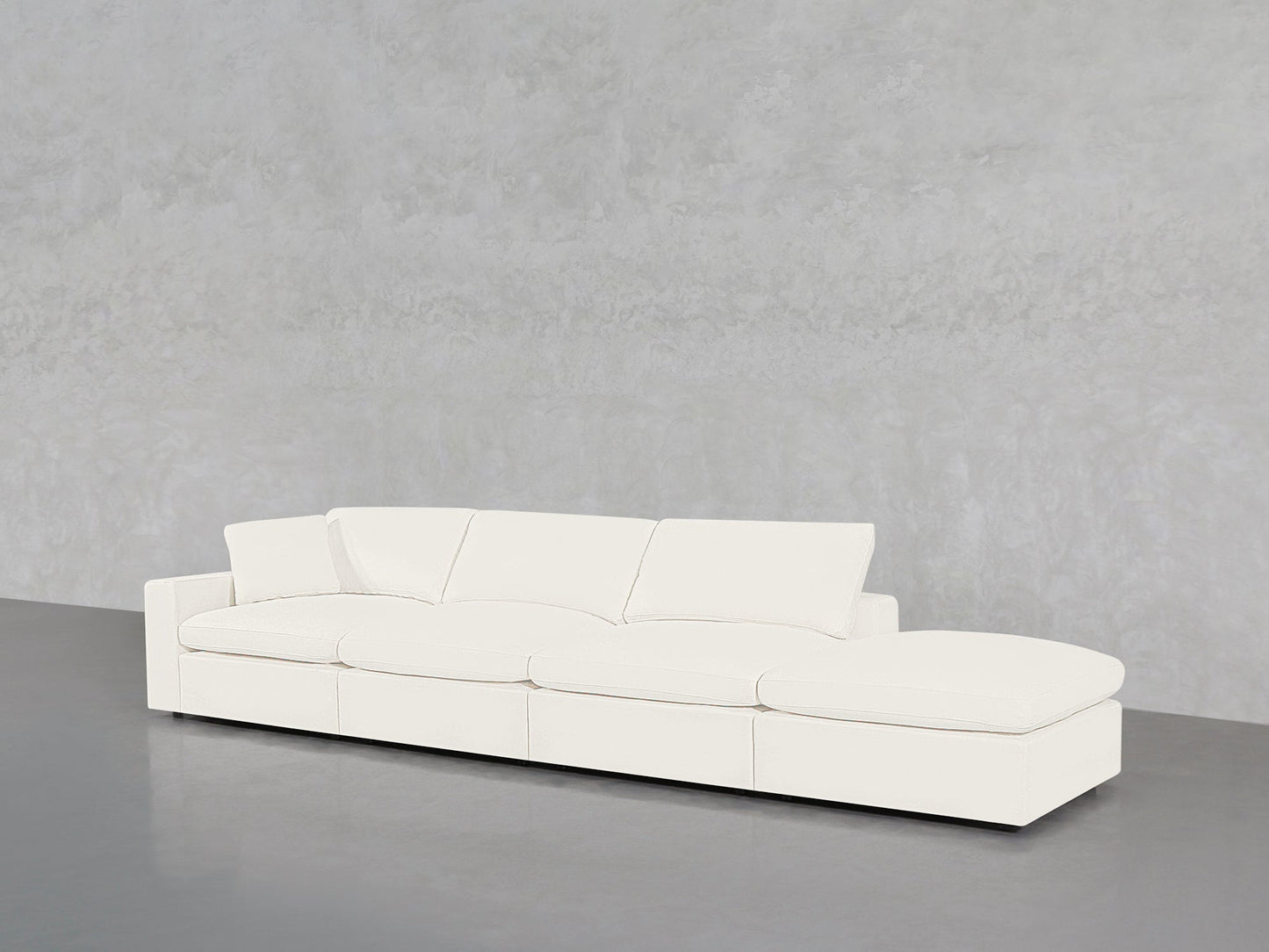 The 4-Seat Modular Lounger Sofa, featuring a modern minimalist design and plush cushions, is placed against a light gray textured wall on a smooth gray floor.