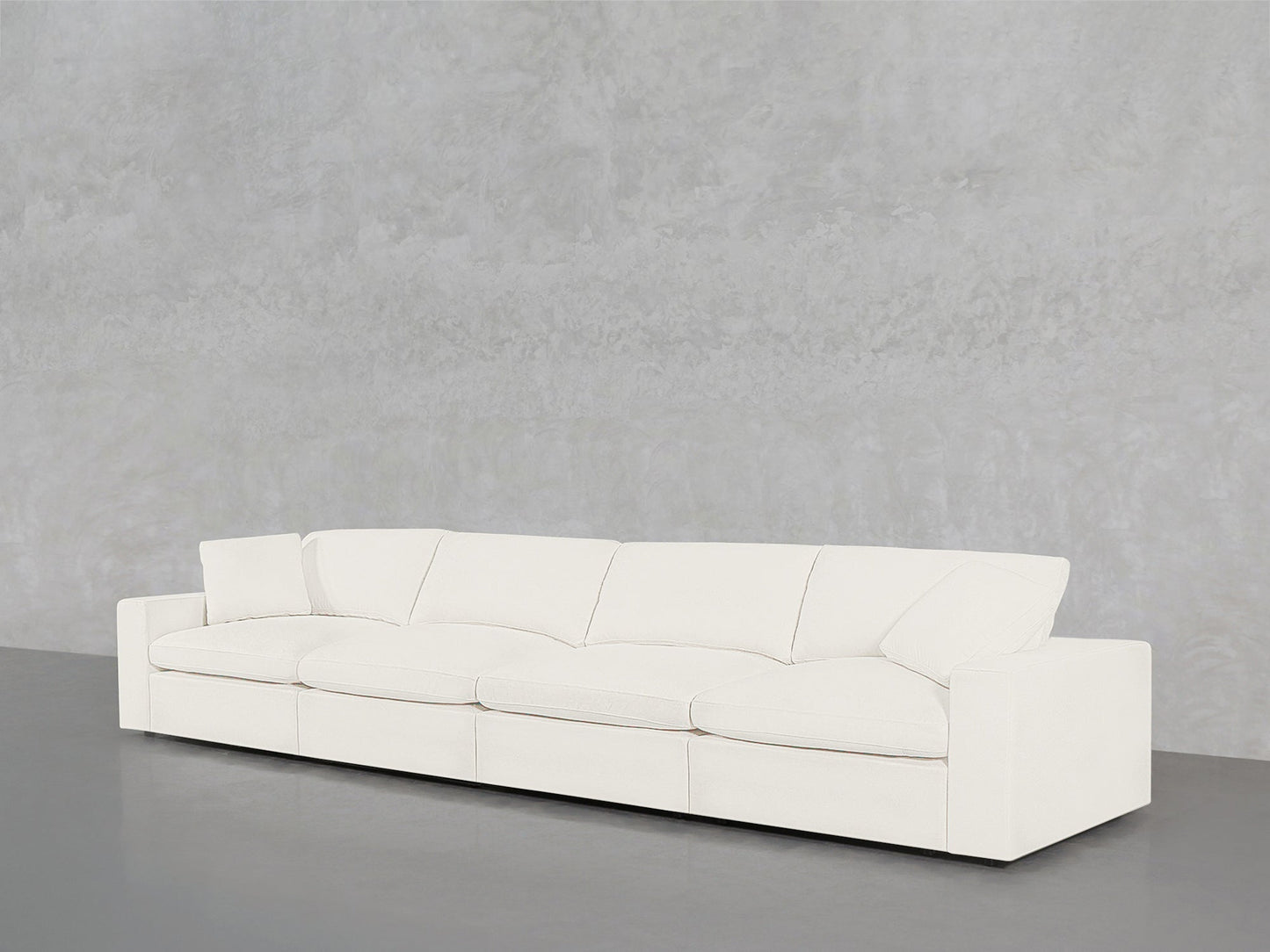 A 4-Seat Modular Sofa in modern white, featuring four seat and back cushions, stands against a plain light gray textured wall on a smooth gray floor.
