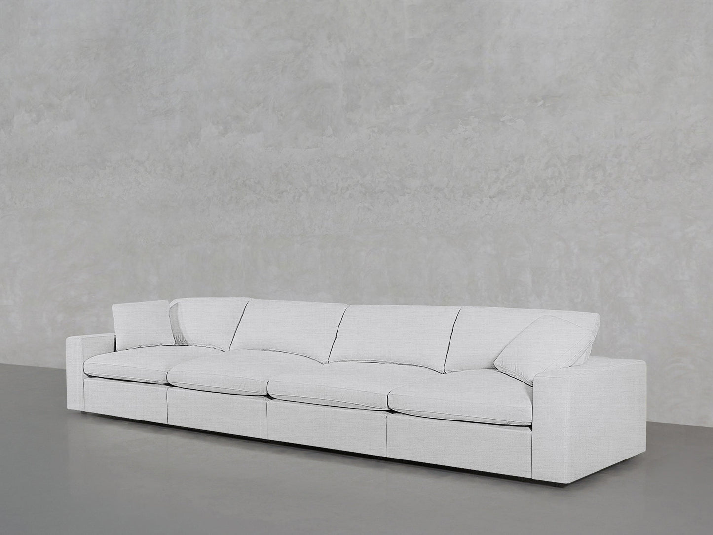 The 4-Seat Modular Sofa, modern and white with four seat cushions and two armrests, sits against a plain light gray textured wall on a smooth gray floor.