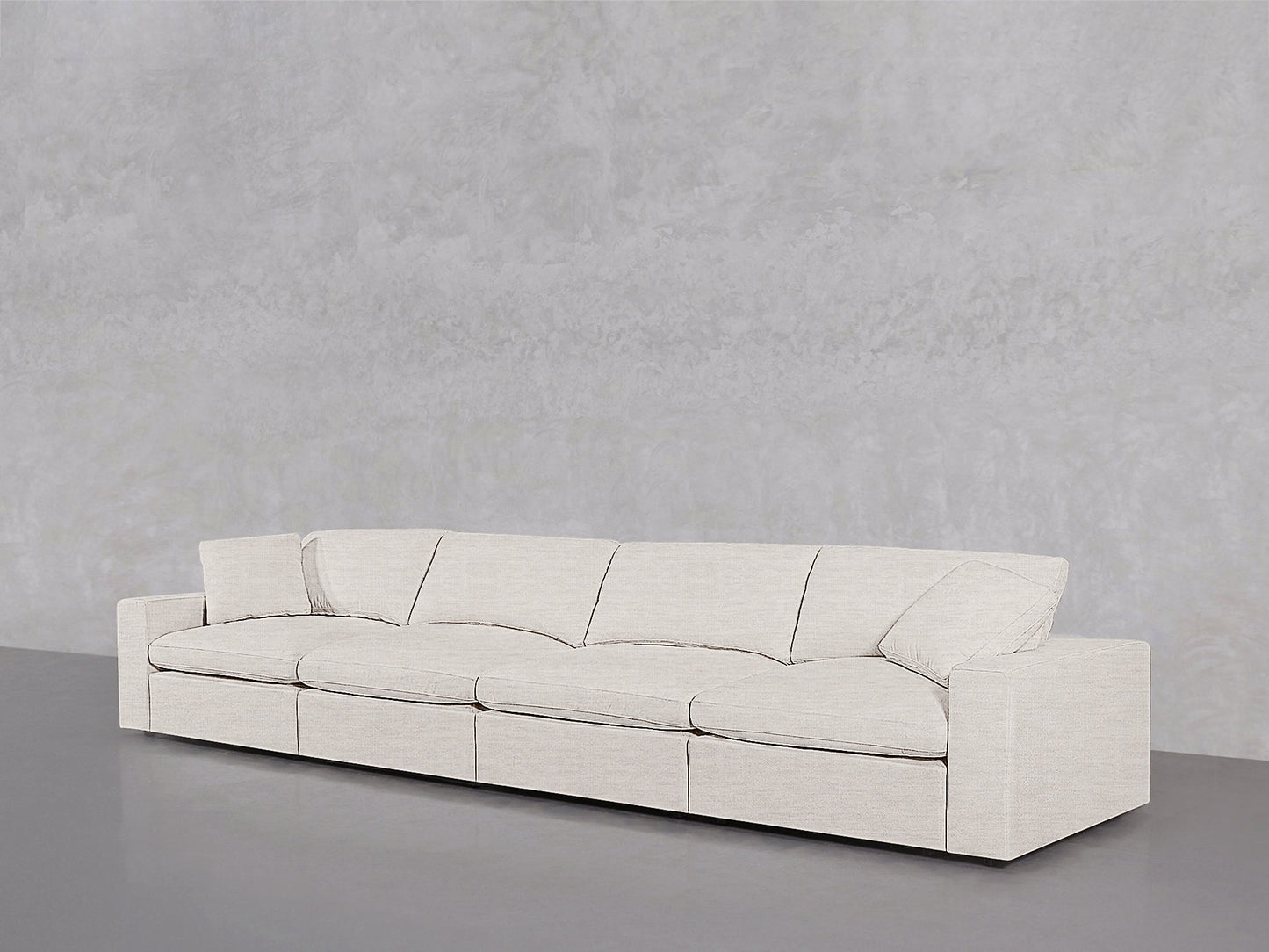 The 4-Seat Modular Sofa, featuring a modern minimalist design in light beige with clean lines and boxy armrests, is positioned against a plain light gray textured wall on a smooth gray floor.