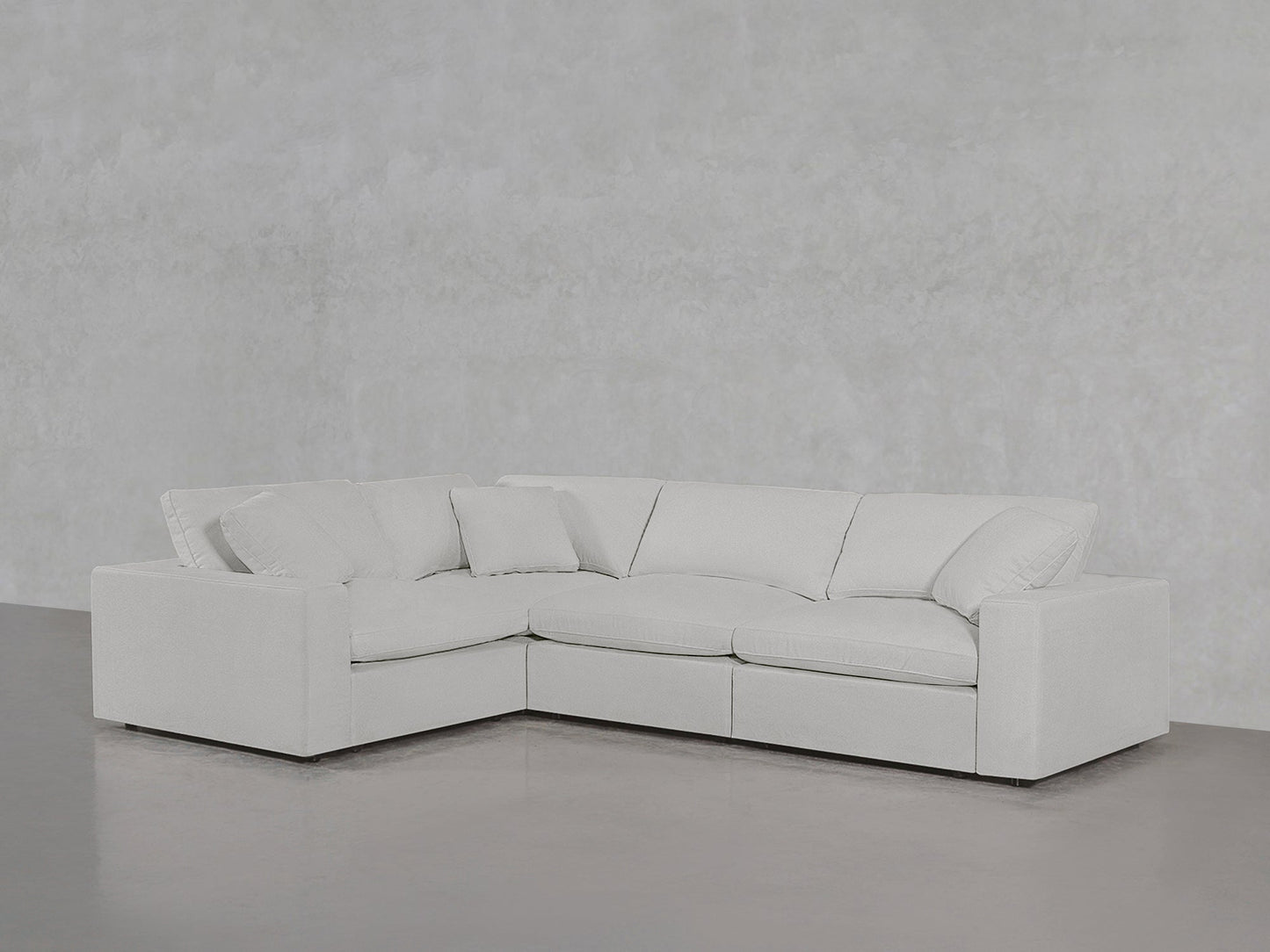 A 4-Seat Modular Corner Sectional in modern light gray with plush cushions sits in a minimalist room featuring light gray walls and a polished concrete floor.