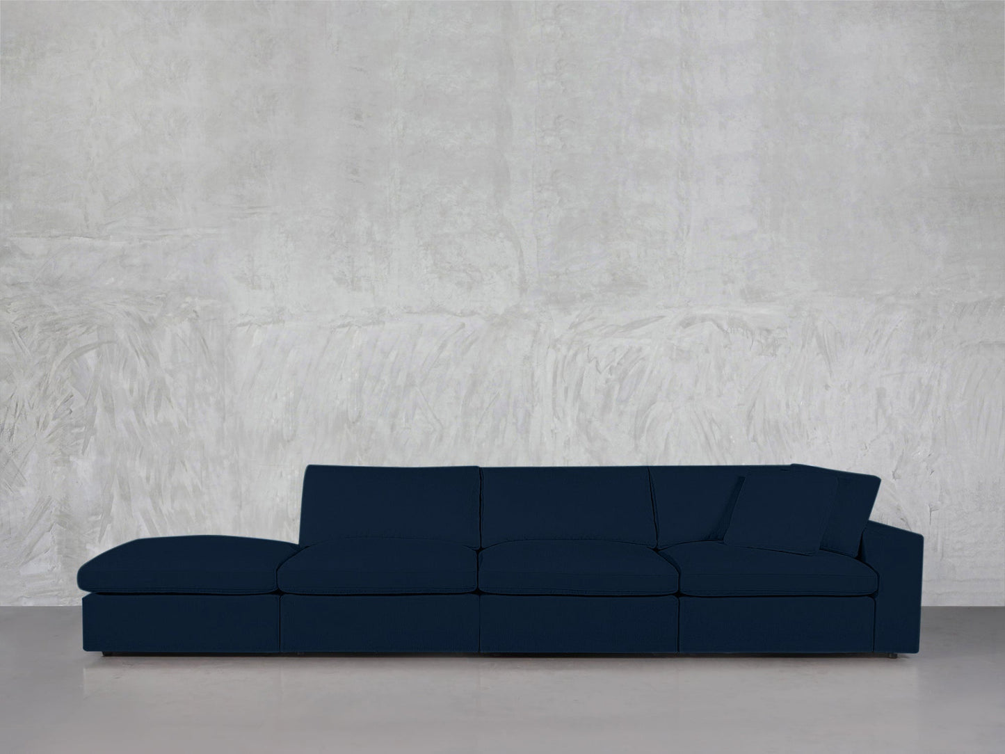 The 4-Seat Modular Lounger Sofa in dark blue features four seat cushions and three back pillows, set against a textured light gray wall atop a smooth, light-toned floor.