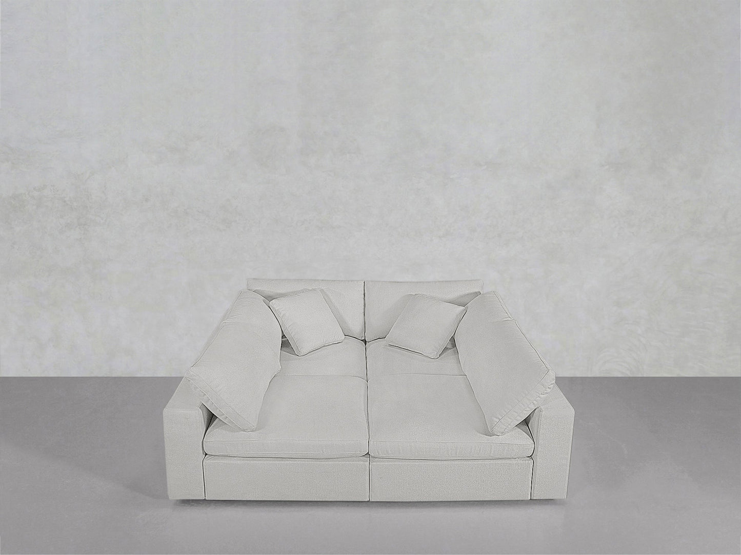 The 4-Seat Modular Pit, featuring wide armrests and four matching cushions, sits against a minimalist light gray wall and floor.