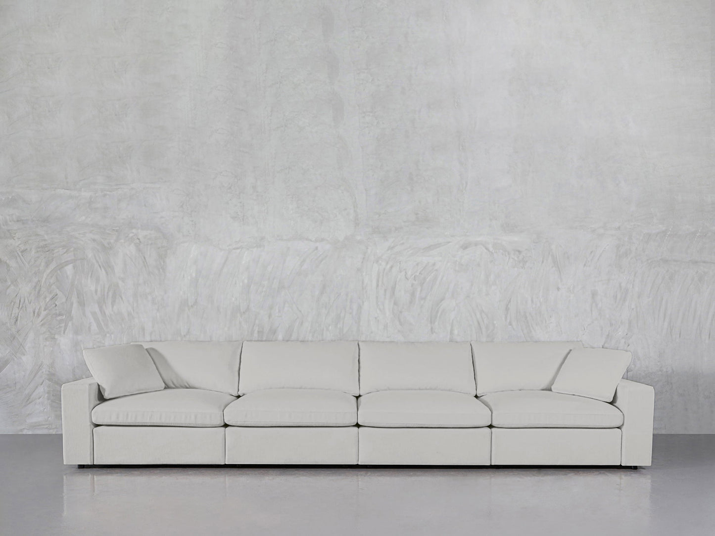 A modern 4-Seat Modular Sofa with square arms and five back cushions in light gray rests against a textured, light wall on a smooth, reflective floor.