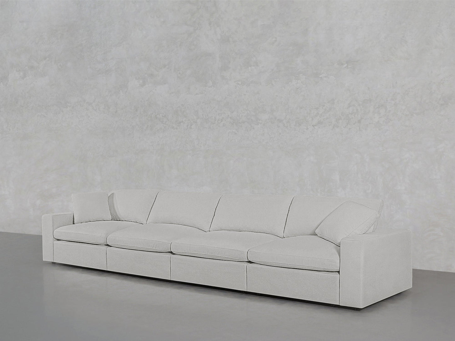 The 4-Seat Modular Sofa, large and modern in light gray with low armrests and four seat cushions, sits against a textured light gray wall on a gray floor.