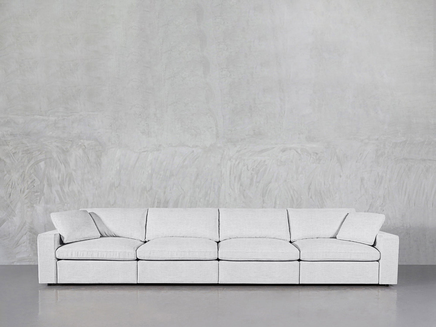 A modern 4-Seat Modular Sofa in light gray with cushions and armrests is placed against a textured gray wall and a smooth gray floor.