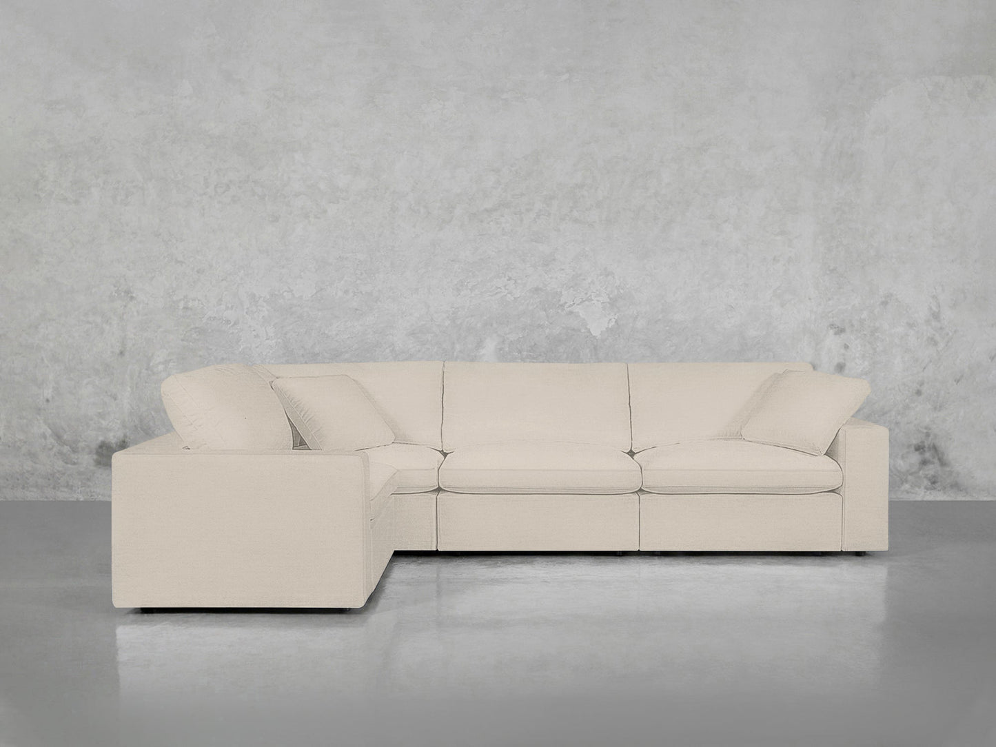 A 4-Seat Modular Corner Sectional in light beige with clean lines and plush cushions is placed against a textured gray wall on a polished gray floor.