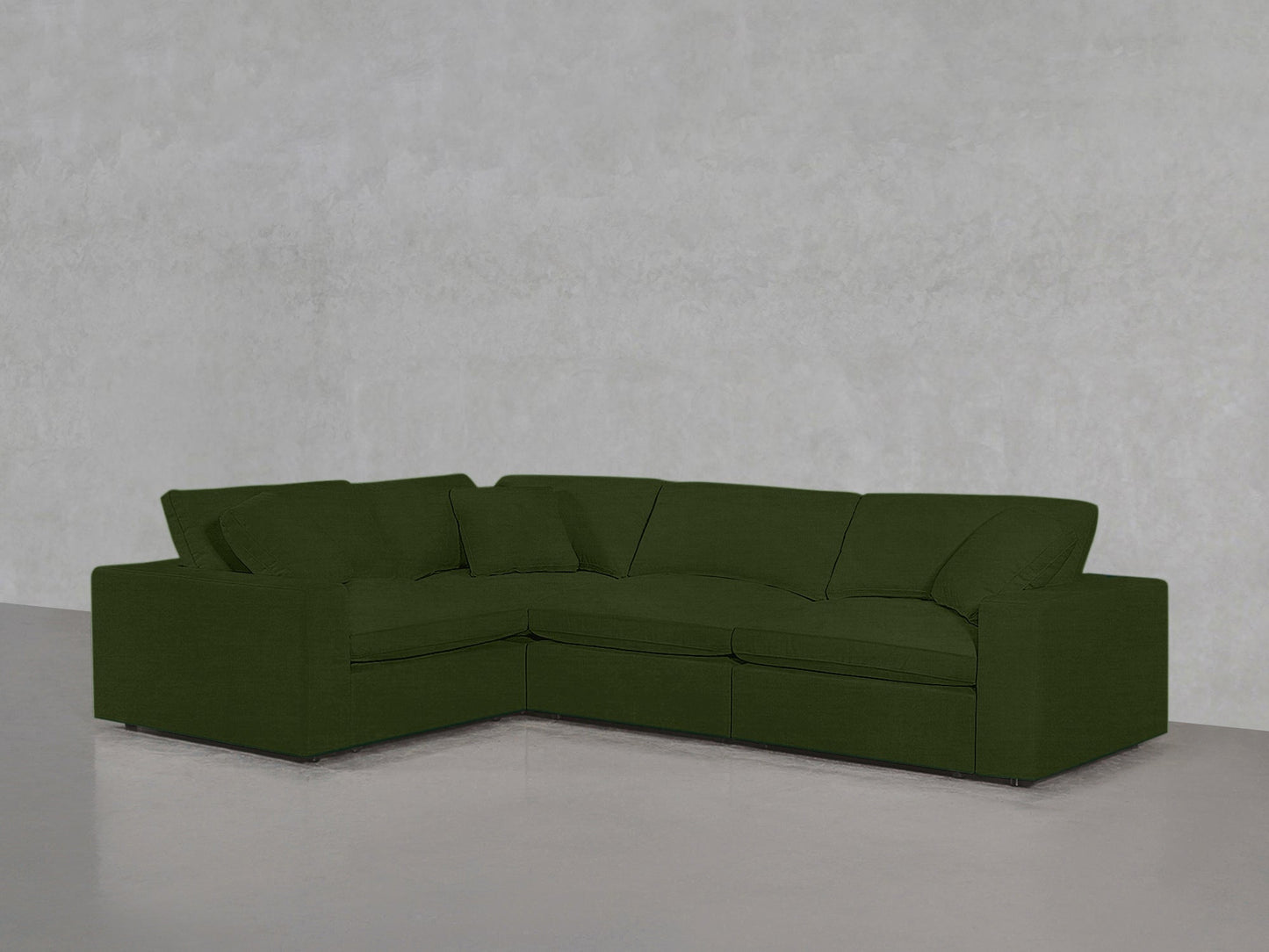 A 4-Seat Modular Corner Sectional in deep green, featuring clean lines and plush cushions, sits on a light gray floor against a textured light gray wall.