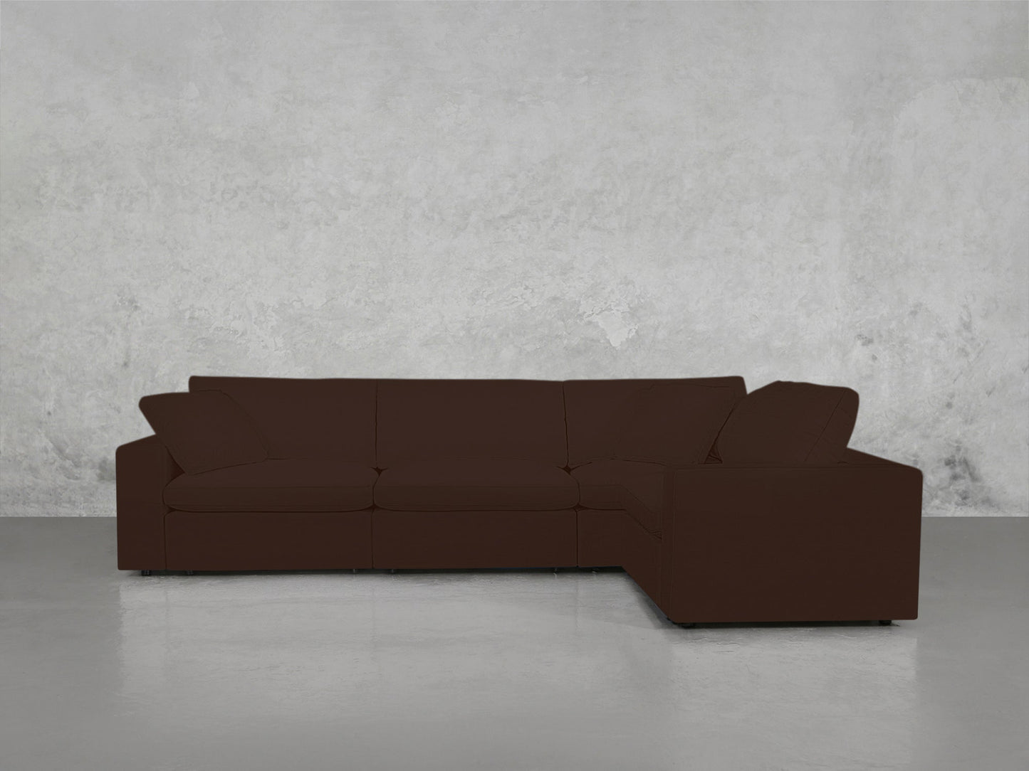 A 4-Seat Modular Corner Sectional in dark brown with a minimalist design is placed against a plain, light gray textured wall on a smooth, light-colored floor.
