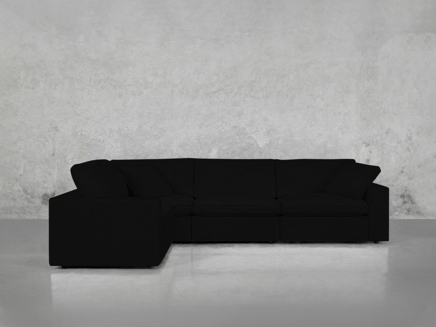 A 4-Seat Modular Corner Sectional in black sits against a light gray textured wall on a polished light floor in a minimalist room.