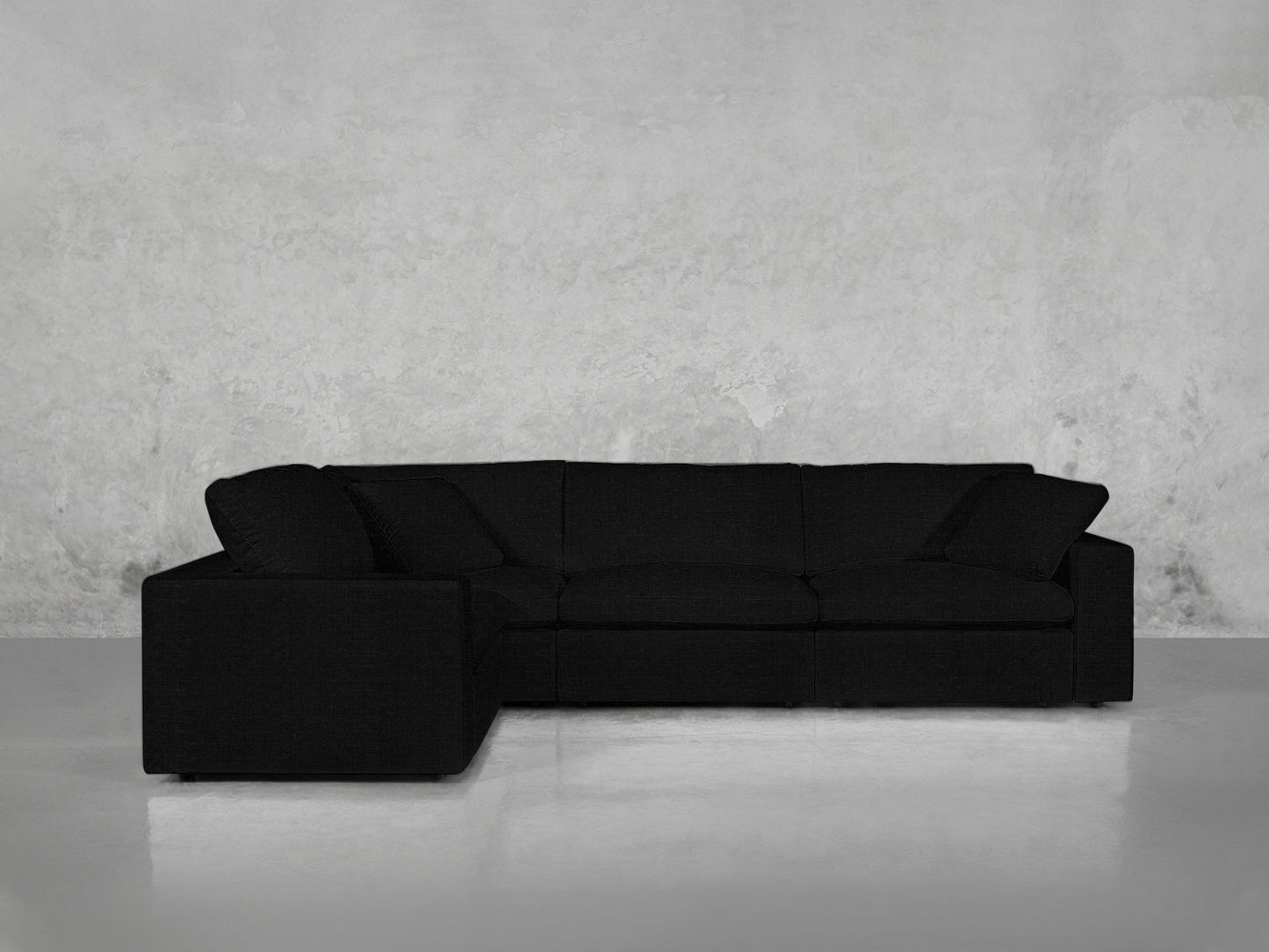 A 4-Seat Modular Corner Sectional with clean lines in modern black rests against a textured light gray wall on a smooth, light-colored floor.