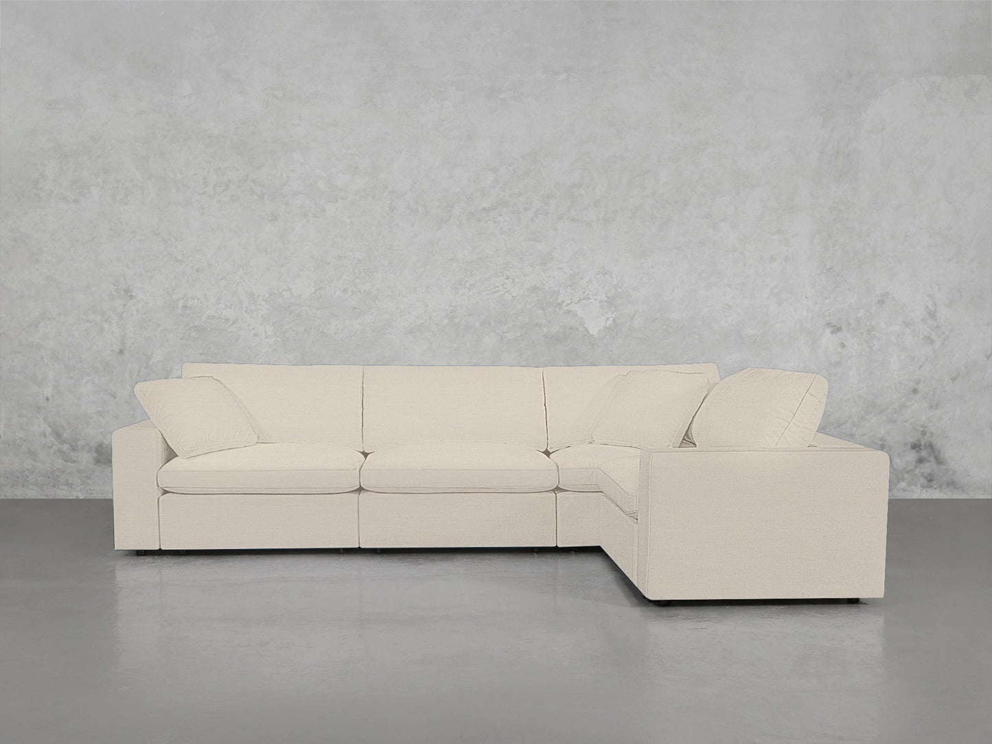 A modern 4-Seat Modular Corner Sectional in light beige with wide armrests and plush cushions sits against a textured gray wall on a smooth gray floor.