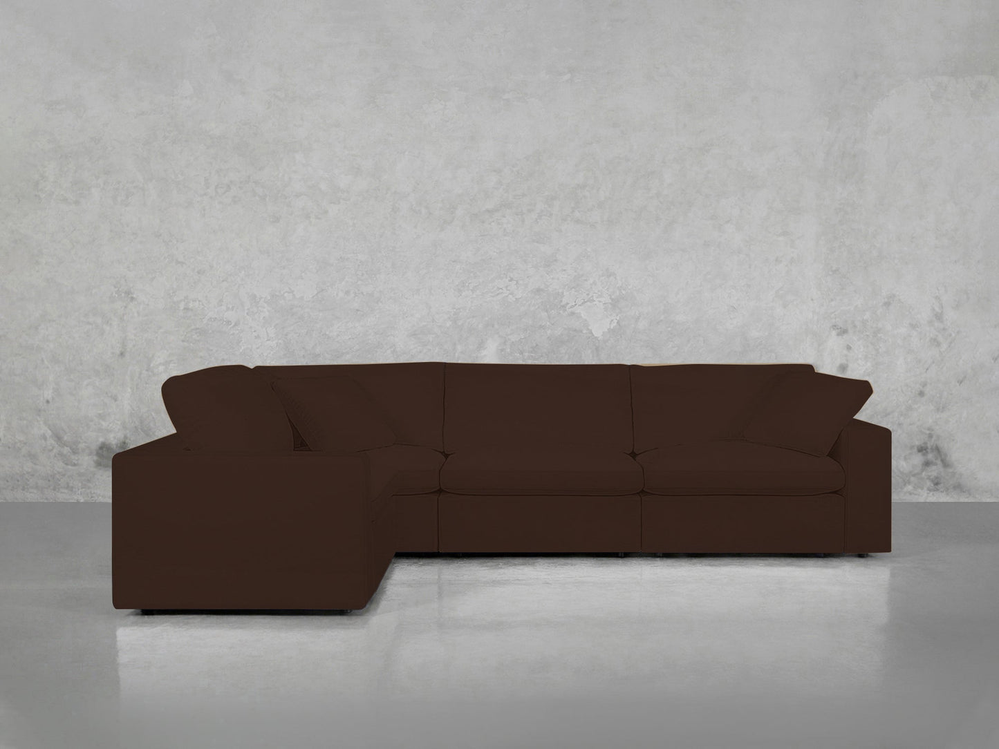 A 4-Seat Modular Corner Sectional in modern dark brown with clean lines and three seat cushions sits in front of a light gray concrete wall and floor.