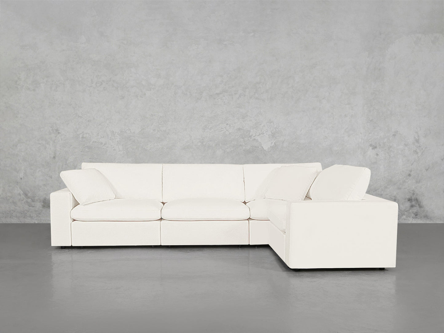 A modern 4-Seat Modular Corner Sectional with clean lines and plush cushions sits on a smooth gray floor against a textured light gray concrete wall.