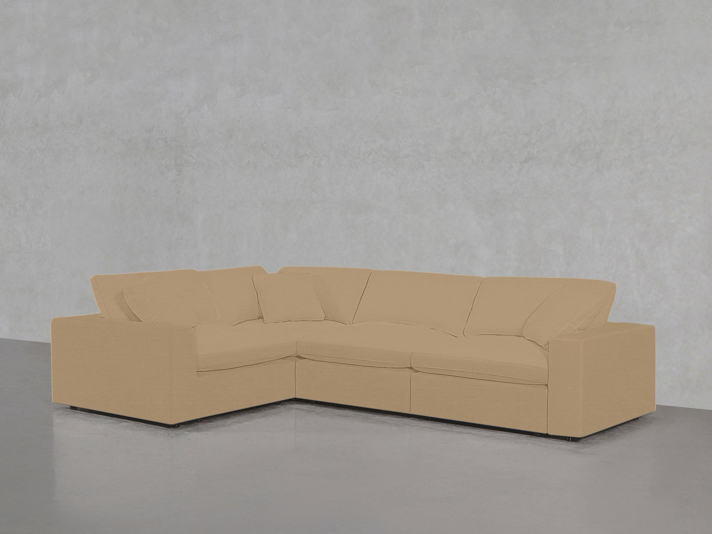 A 4-Seat Modular Corner Sectional in beige with plush cushions is arranged against a plain, light gray textured wall and a smooth gray floor.