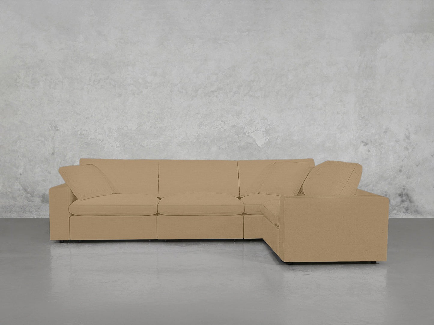 A 4-Seat Modular Corner Sectional in beige with cushions and wide armrests is set against a textured light gray concrete wall on a smooth gray floor.
