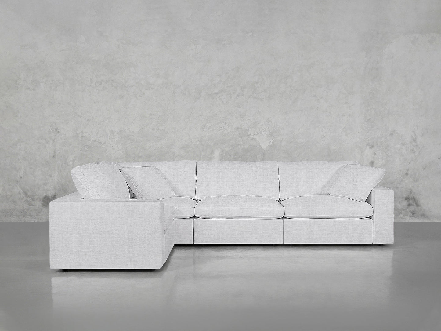 A modern 4-Seat Modular Corner Sectional in light gray, featuring three seat cushions and two back cushions, sits against a plain textured gray wall on a smooth, shiny floor.