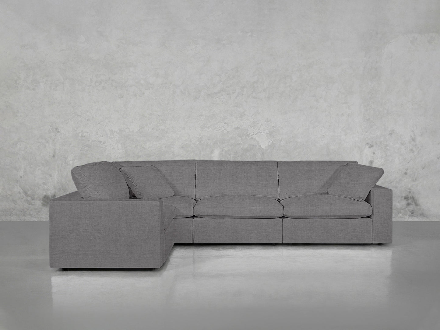 A 4-Seat Modular Corner Sectional in modern gray is set against a textured light gray wall on a glossy floor, with matching three seat and back cushions.