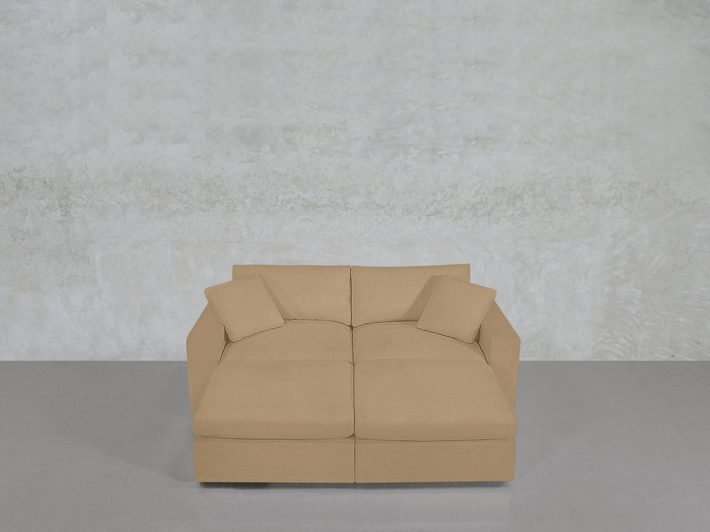A modern 4-Seat Modular Daybed with two matching square cushions sits on a smooth gray floor against a textured light gray wall.