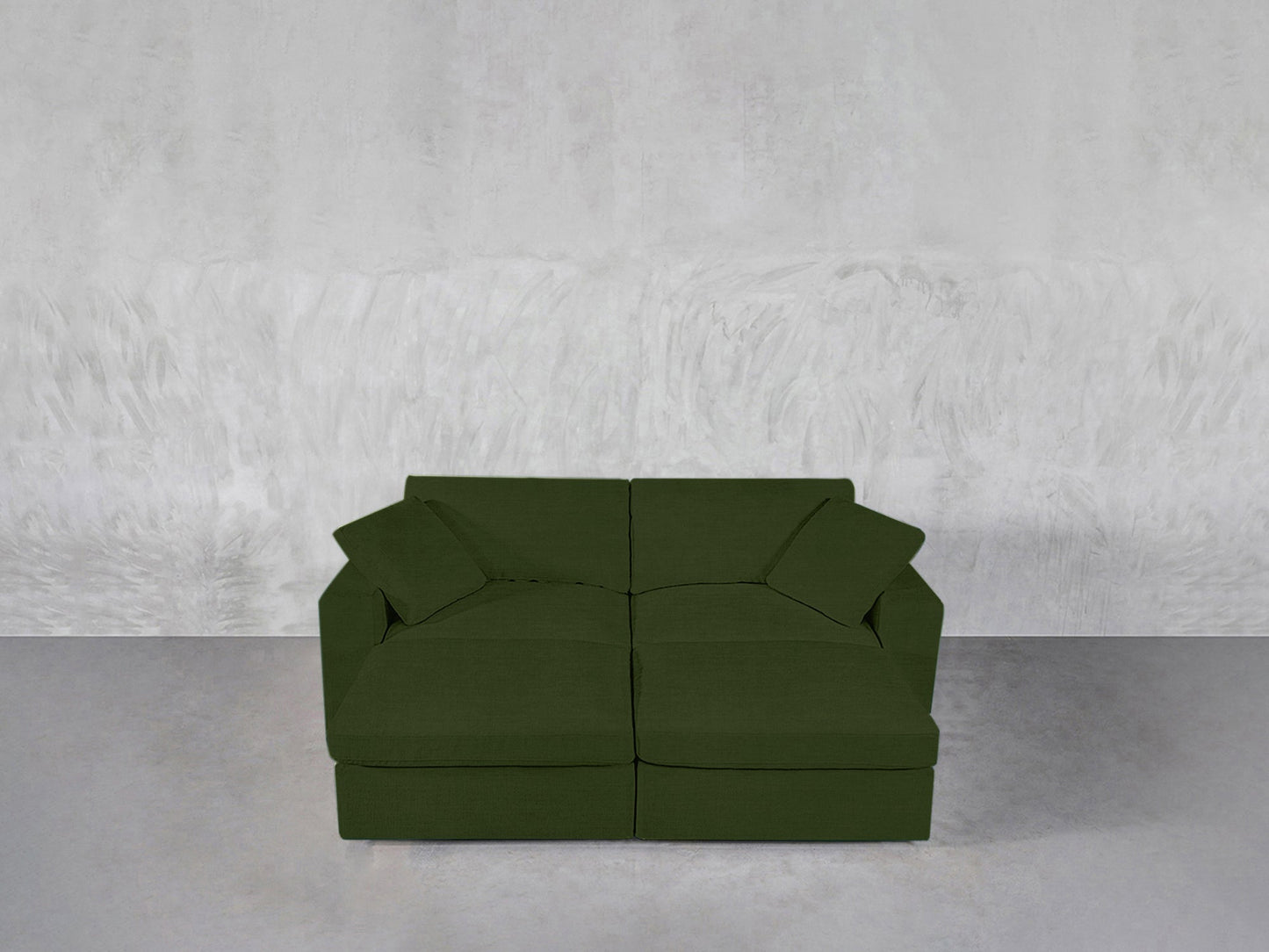 A 4-Seat Modular Daybed in dark green with two matching cushions rests on a smooth, light gray floor against a textured, light gray wall.