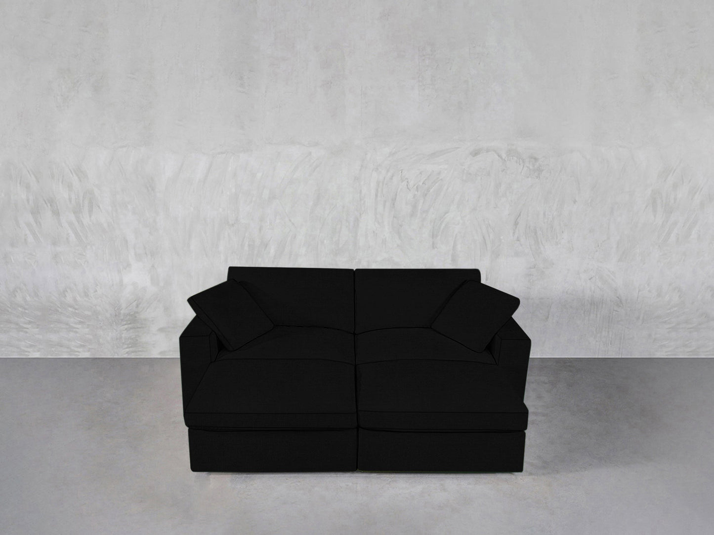 A 4-Seat Modular Daybed in sleek black with two matching cushions is placed on a gray concrete floor against a textured light gray wall.