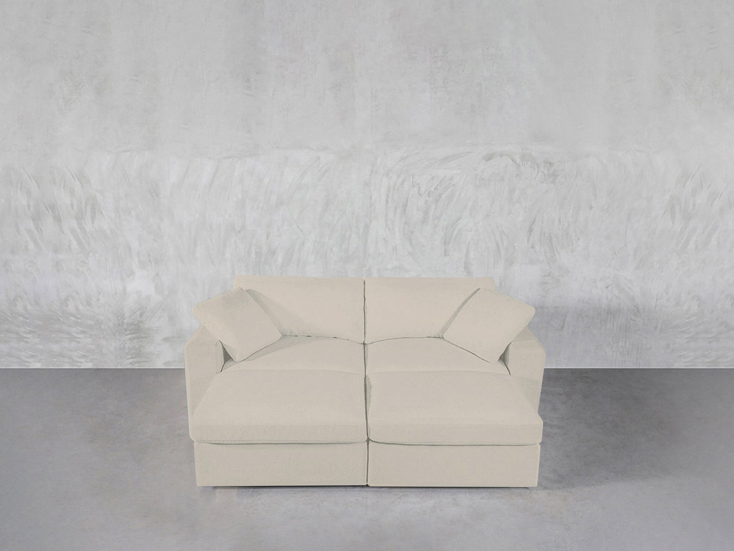 A modern light beige 4-Seat Modular Daybed with two matching cushions is placed against a textured light gray wall on a smooth gray floor.