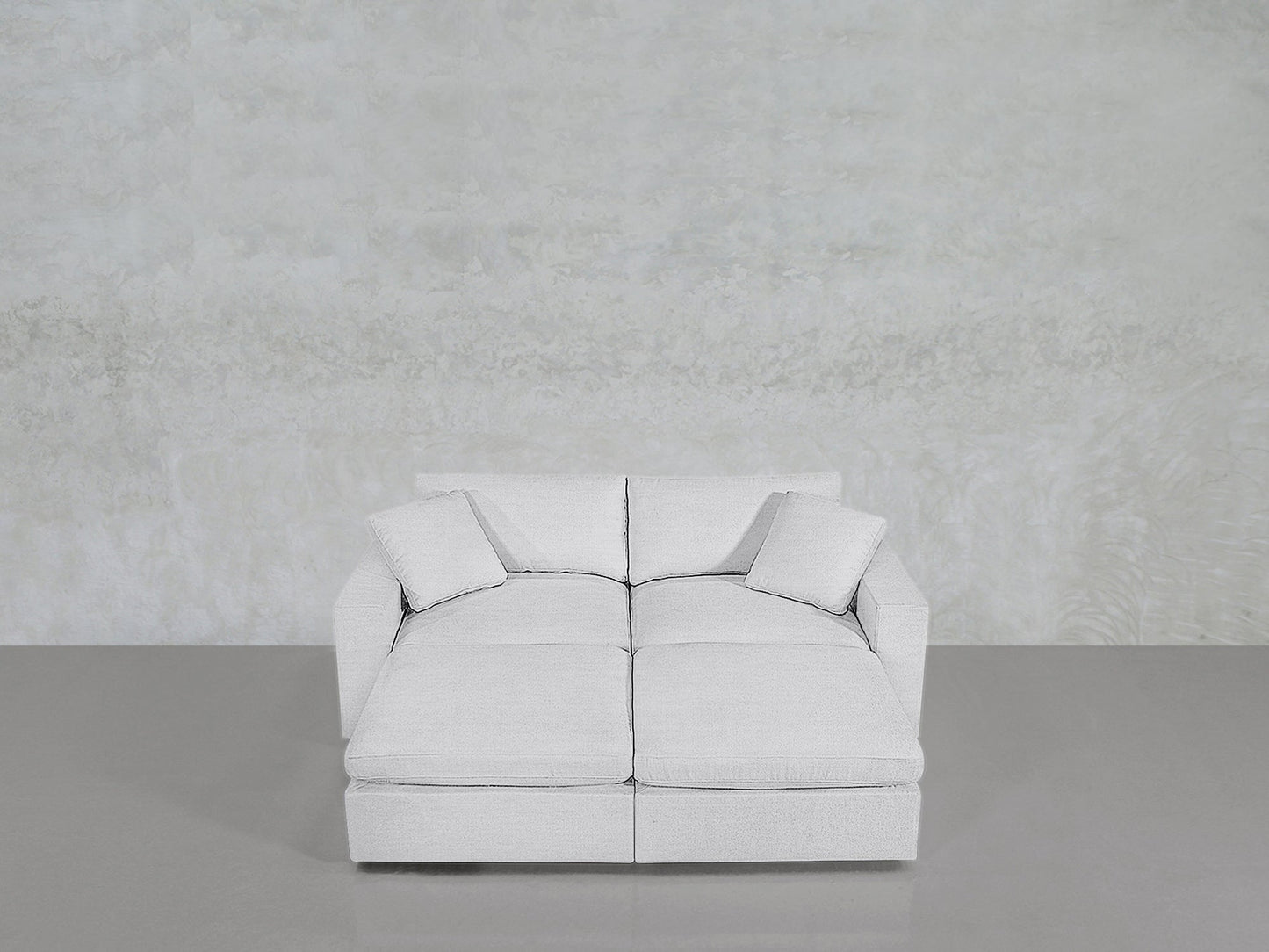 The 4-Seat Modular Daybed in light gray features two seat cushions and two matching throw pillows, positioned on a smooth gray floor against a textured, light gray wall.
