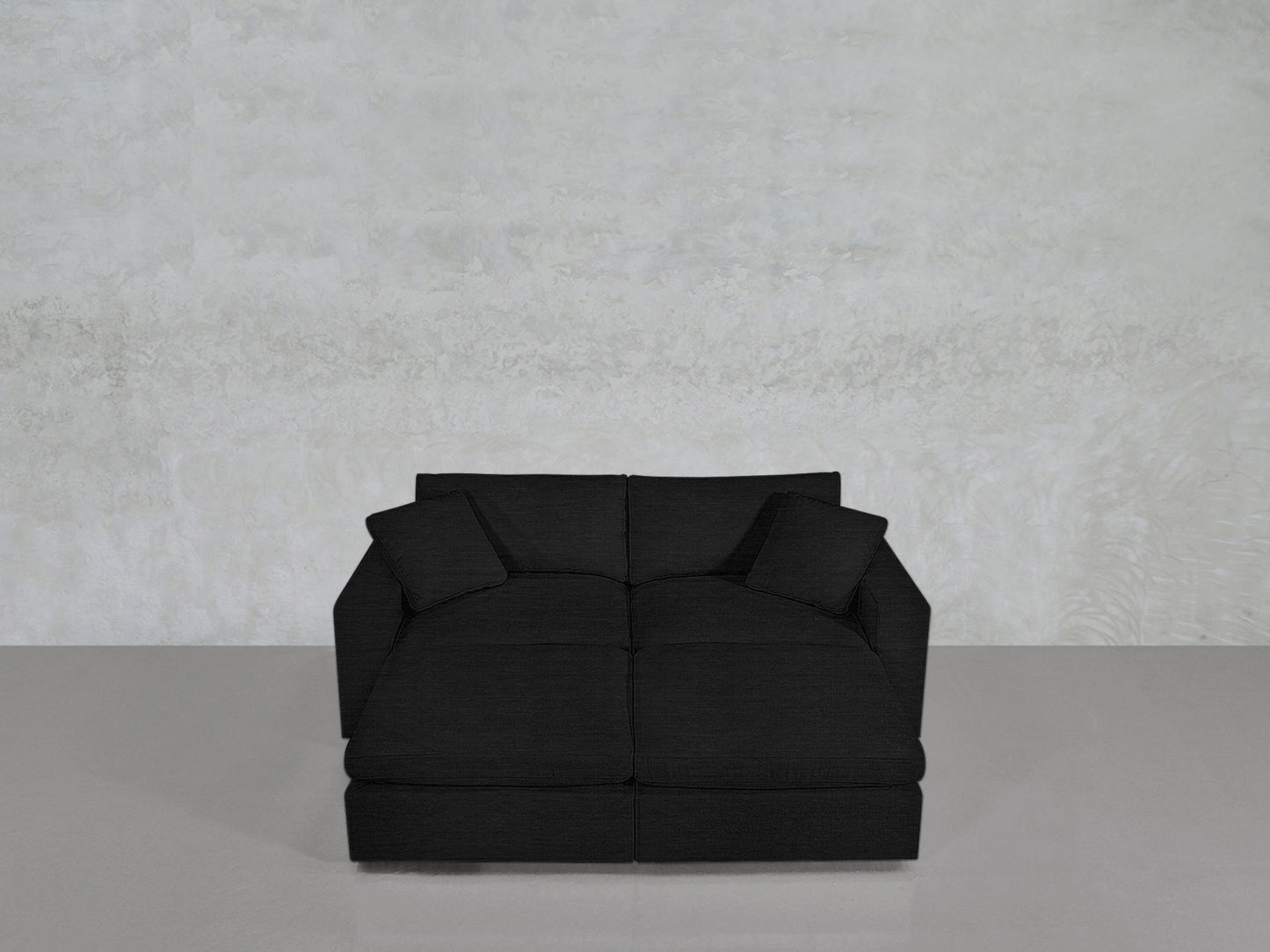 A 4-Seat Modular Daybed in modern black with two matching cushions is set on a glossy light gray floor against a textured light gray wall.