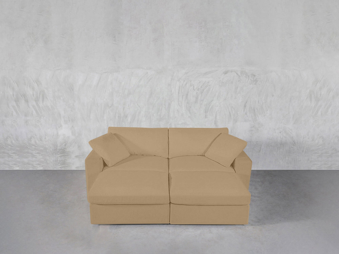 A beige 4-Seat Modular Daybed with square armrests and two matching cushions sits against a light gray textured wall on a smooth gray floor.