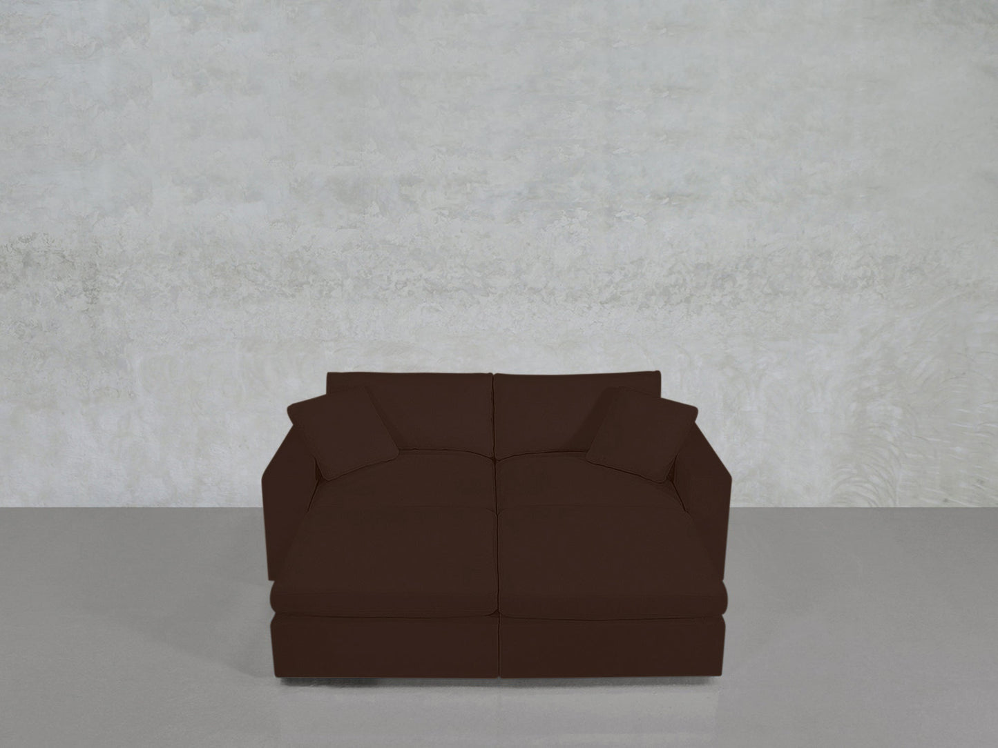 A 4-Seat Modular Daybed in dark brown with two matching cushions sits on a light gray floor against a textured, off-white wall.