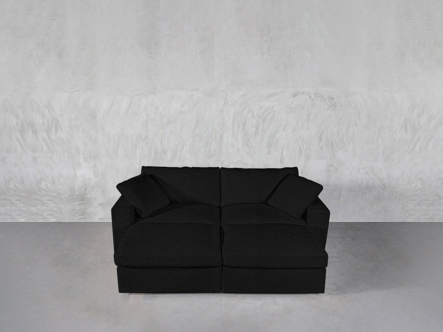 A contemporary black 4-Seat Modular Daybed with plush cushions and armrests, displayed against a light gray textured wall and a smooth gray floor.