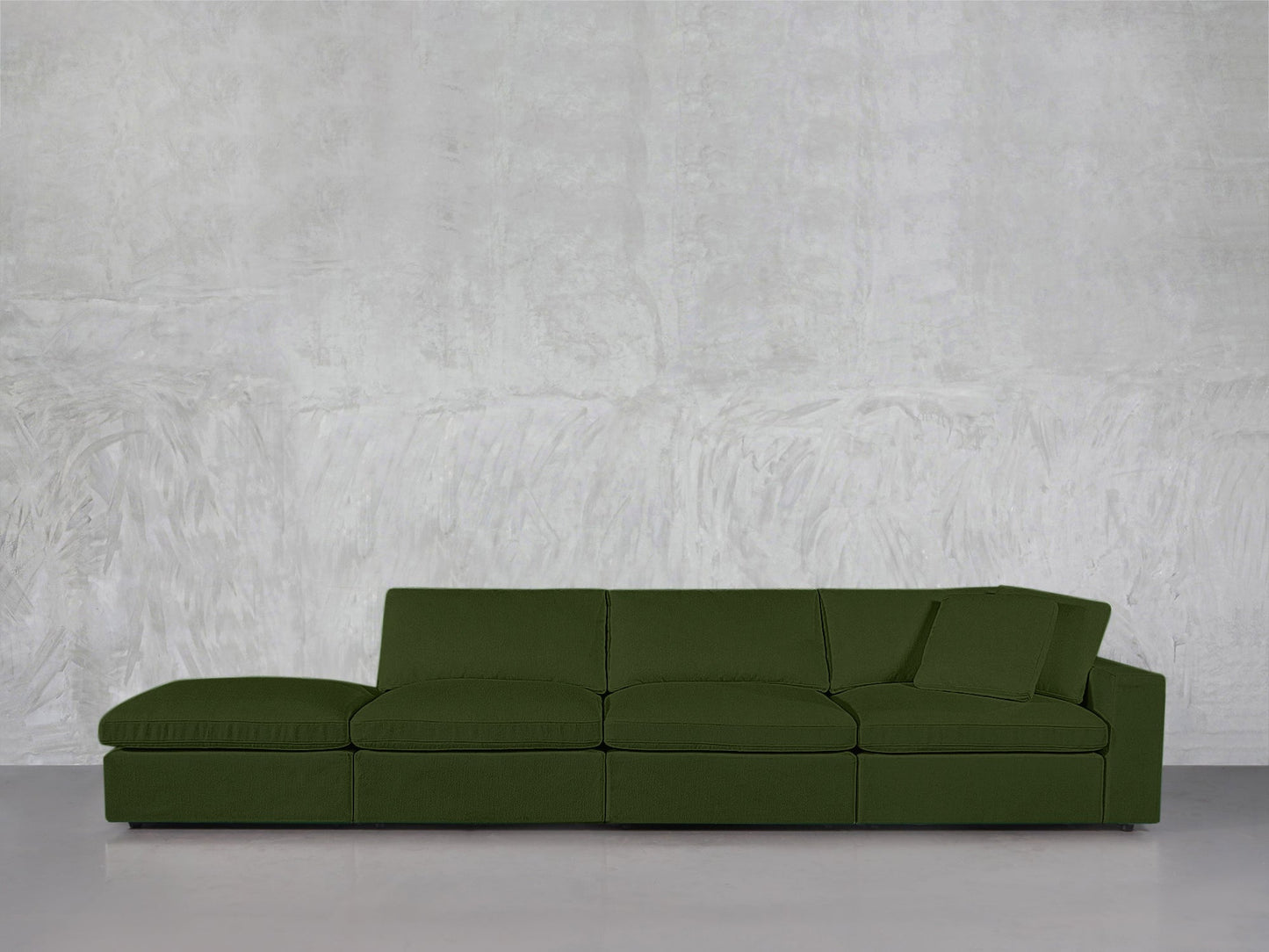 The 4-Seat Modular Lounger Sofa in green with one armrest sits against a plain, light gray textured wall on a gray floor.
