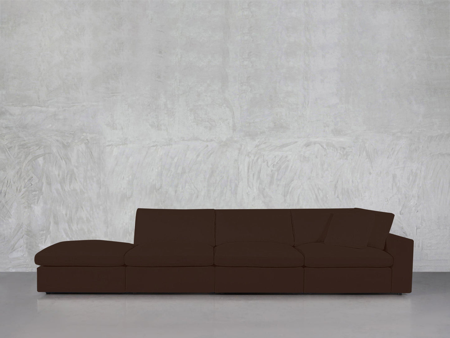 A 4-Seat Modular Lounger Sofa with a chaise, in modern dark brown, is placed against a textured light gray wall on a smooth concrete floor.