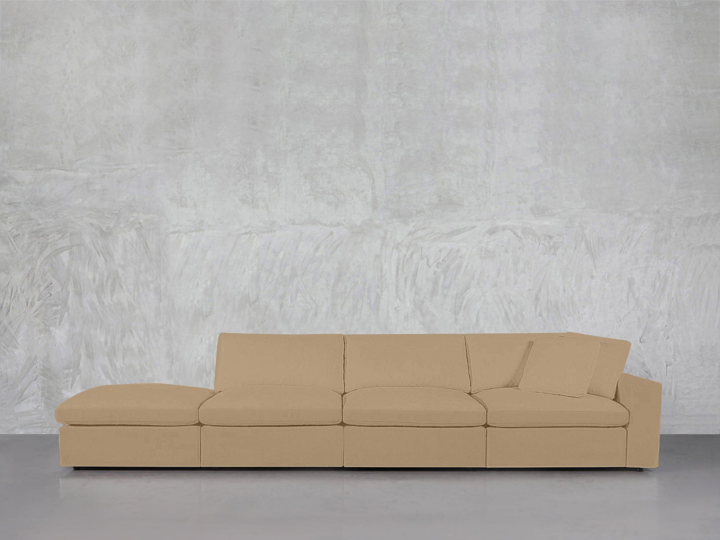 The 4-Seat Modular Lounger Sofa features a modern beige design with clean lines and a single matching cushion, set against a textured light gray wall and smooth gray floor.