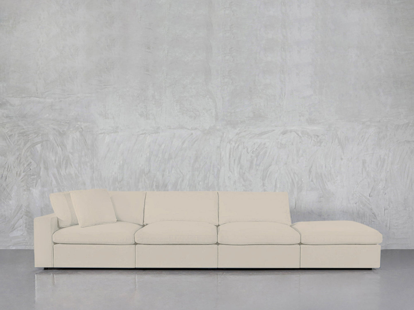 A modern 4-Seat Modular Lounger Sofa in light beige, featuring four seat cushions and one matching pillow, set against a textured pale gray wall on a shiny gray floor.