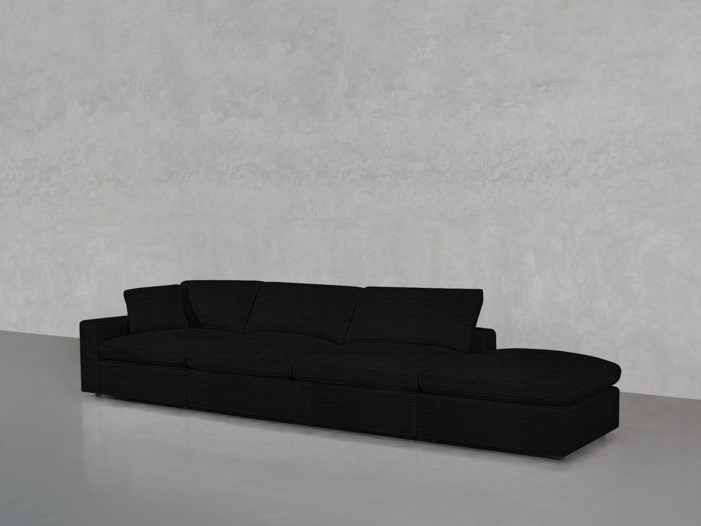 A 4-Seat Modular Lounger Sofa in black with wide cushions and a right-side chaise, placed against a plain light gray wall and floor.