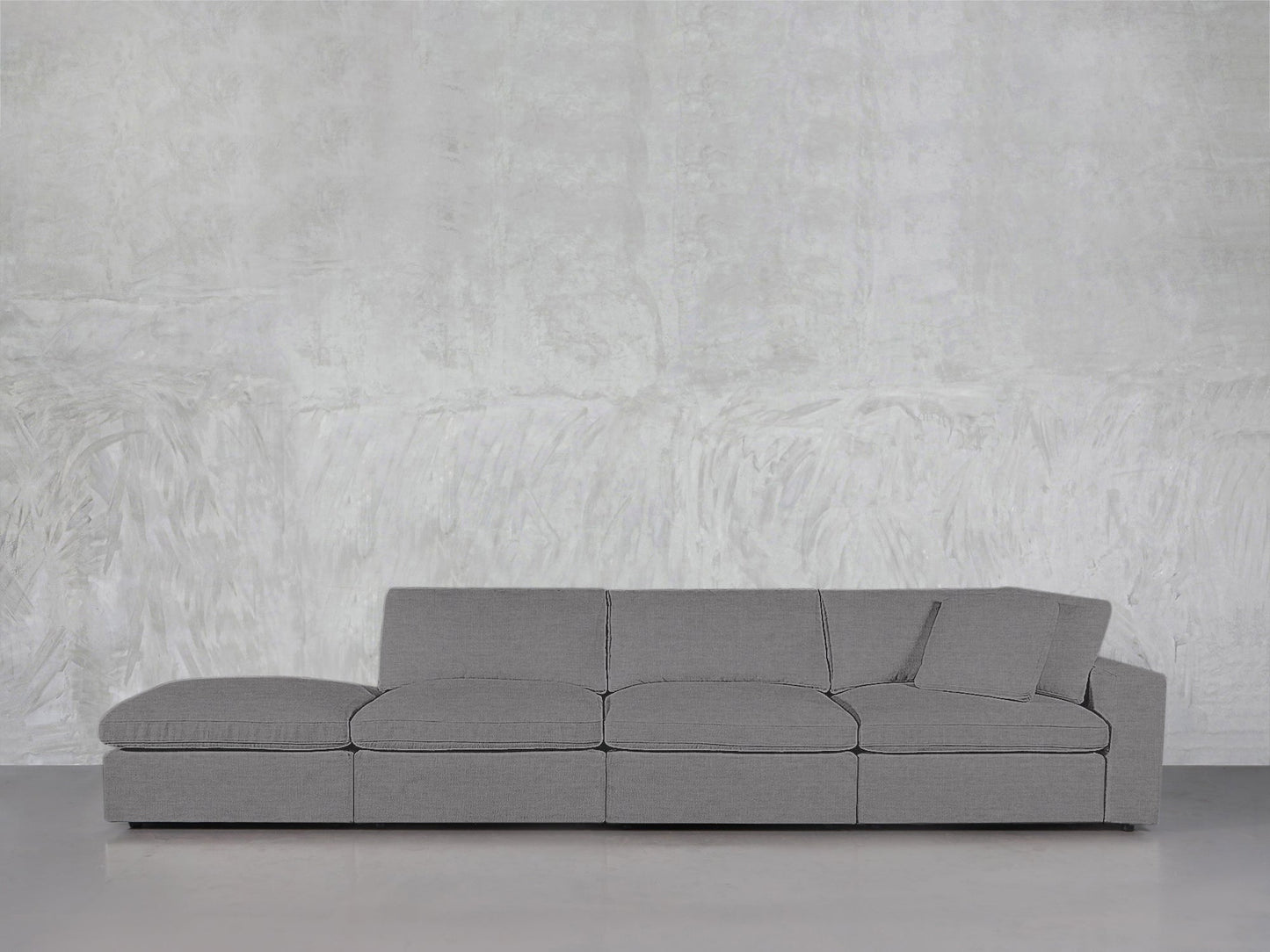 A modern gray 4-Seat Modular Lounger Sofa with matching pillow is arranged against a textured light gray wall and a smooth floor.