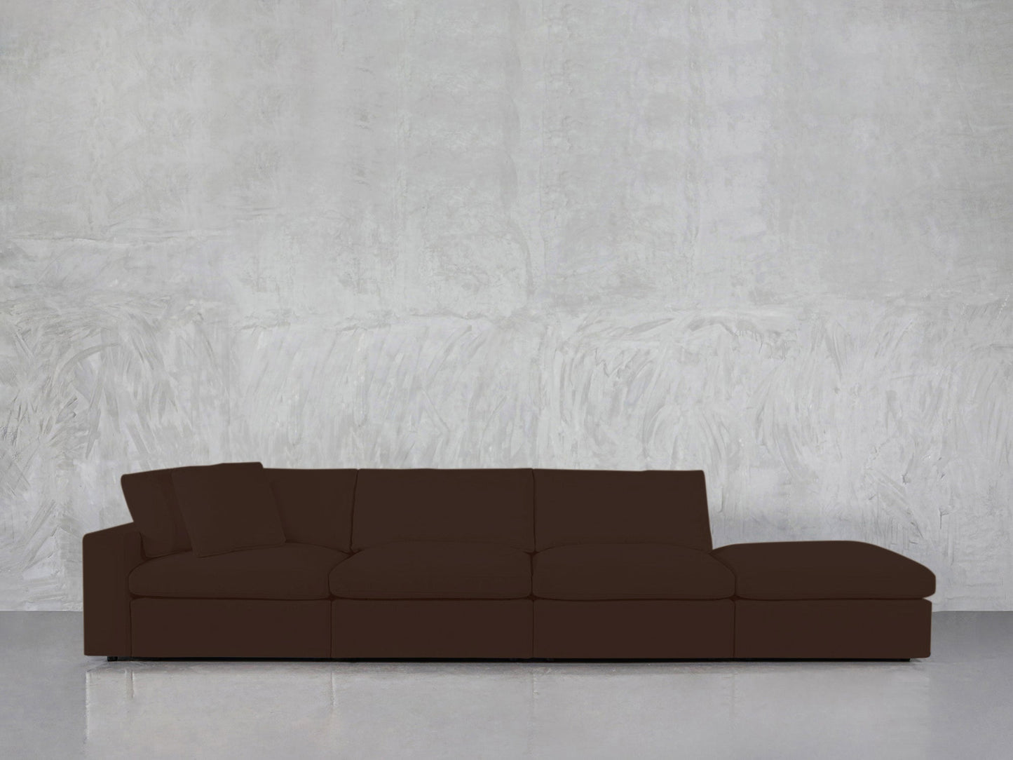 The 4-Seat Modular Lounger Sofa, featuring a modern design in dark brown with a low back and one armrest, is placed before a textured light gray wall and a shiny floor.