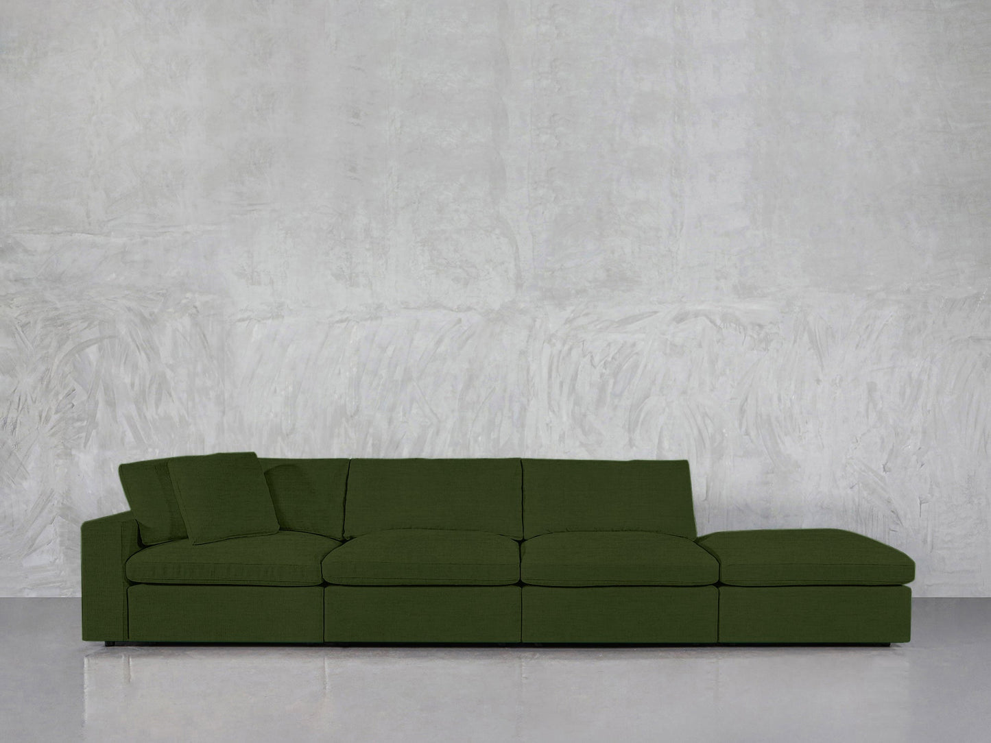 The 4-Seat Modular Lounger Sofa in green features four seats and a matching cushion, placed against a textured light gray wall and glossy gray flooring.