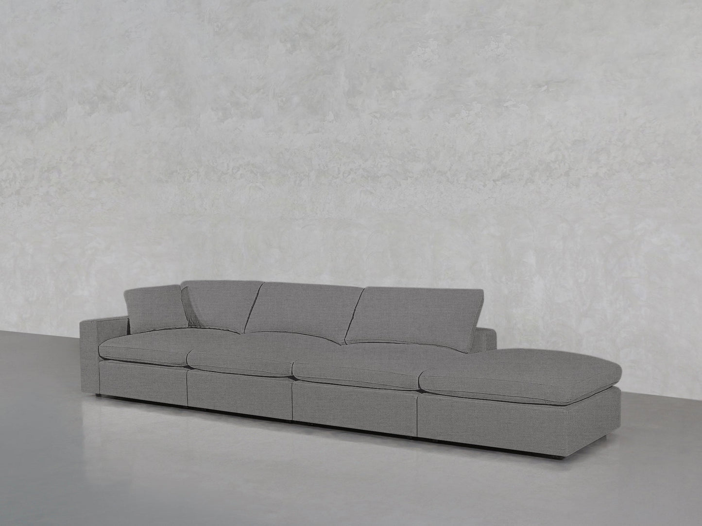 The 4-Seat Modular Lounger Sofa features a modern grey design with three seat cushions and a right-side extended chaise, set against a light grey textured wall and smooth grey flooring.