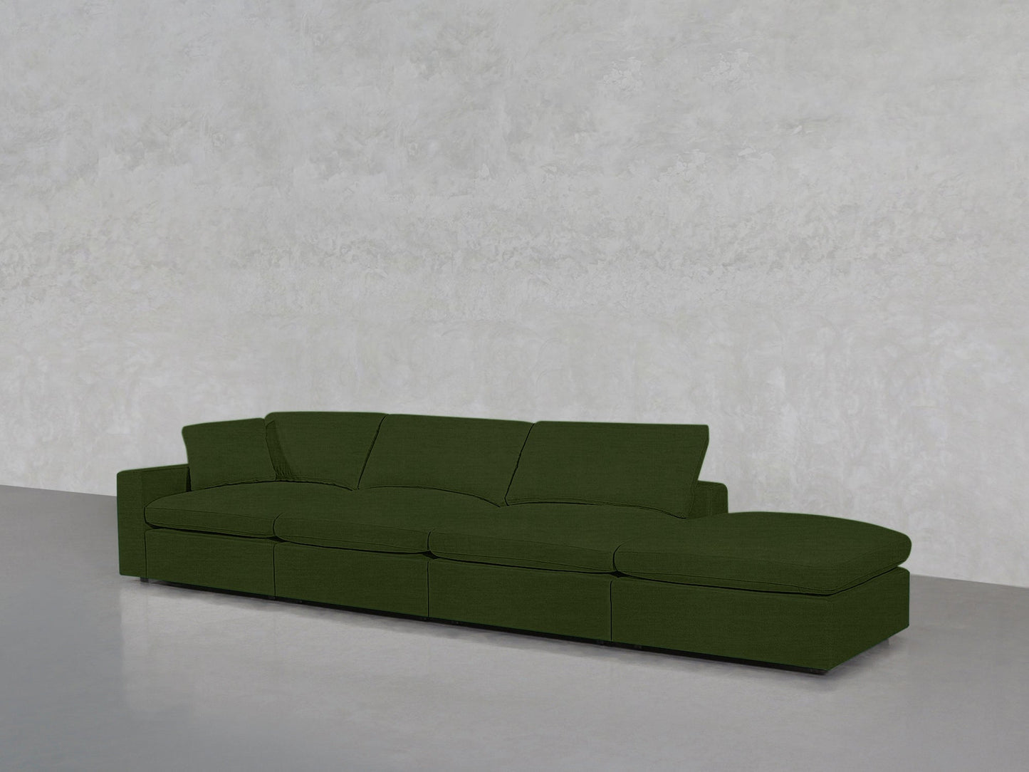 The 4-Seat Modular Lounger Sofa in green features wide cushions and a right-side chaise, set against a plain light gray textured wall and floor.
