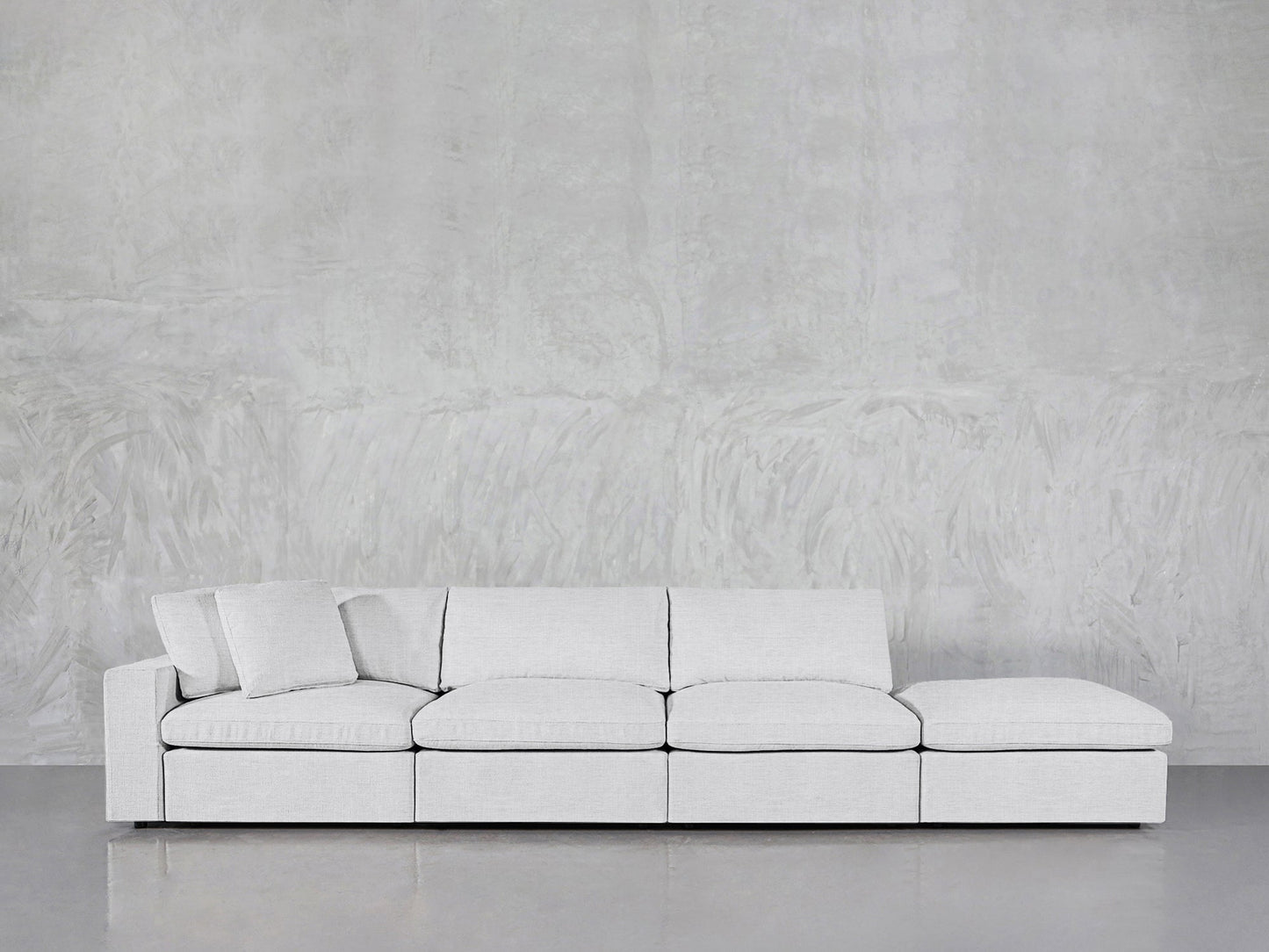 The 4-Seat Modular Lounger Sofa in light gray features four square seat cushions and one matching pillow, showcased against a textured gray wall and a smooth gray floor.