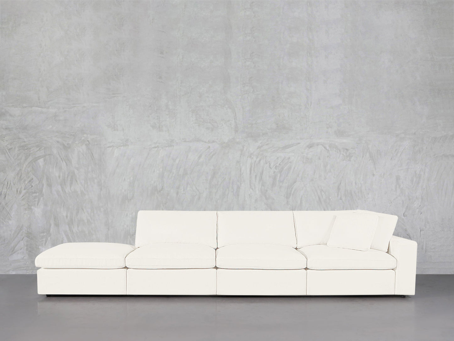 The 4-Seat Modular Lounger Sofa in white, featuring a pillow on one end, is set against a textured light gray wall and smooth gray floor for a contemporary minimalist look.