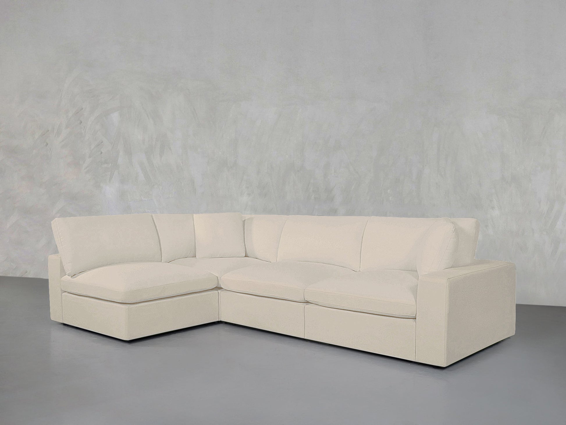 The 4-Seat Modular Open Corner Sectional features a modern L-shaped design with plush cushions in beige, displayed against a minimalist light gray wall and floor.