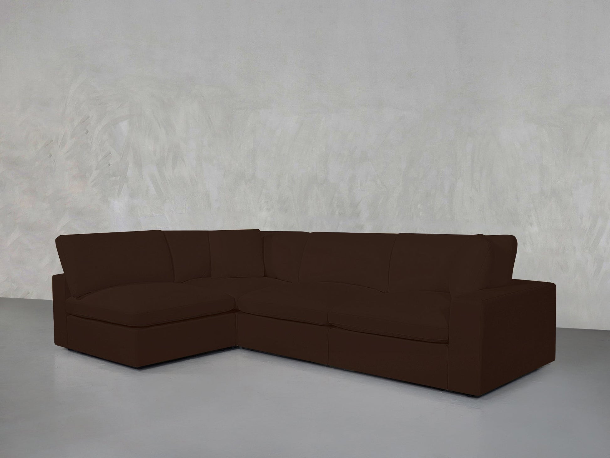 A 4-Seat Modular Open Corner Sectional in dark brown forms an L-shape in an empty room with light gray textured walls and a smooth, light gray floor.