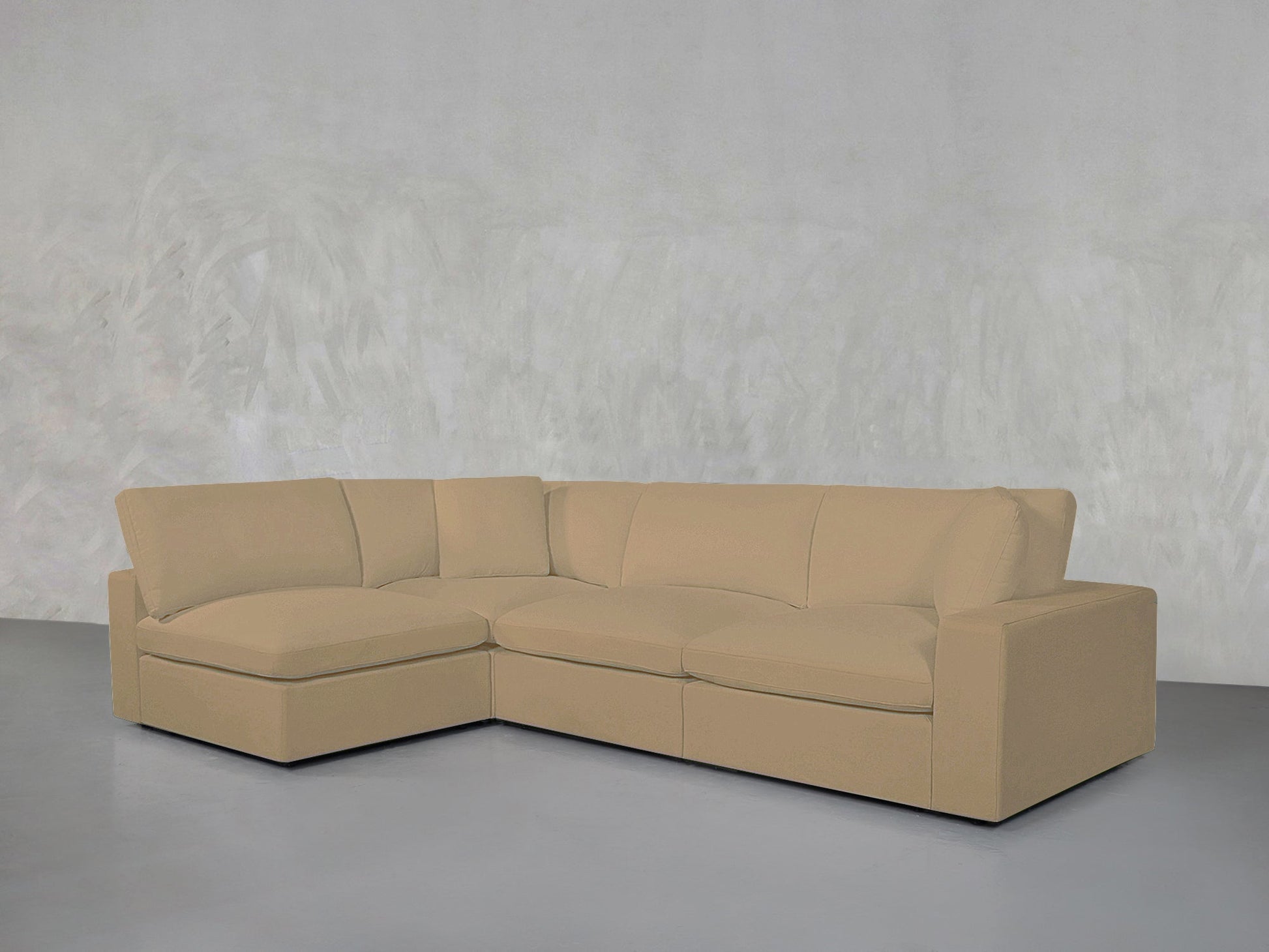 The 4-Seat Modular Open Corner Sectional in beige sits against a plain, light gray textured wall on a gray floor, creating a minimalist setting.