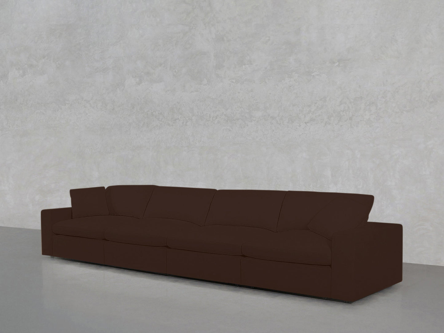 The 4-Seat Modular Sofa in dark brown, featuring four seat cushions and wide armrests, sits against a light gray textured wall on a smooth gray floor.
