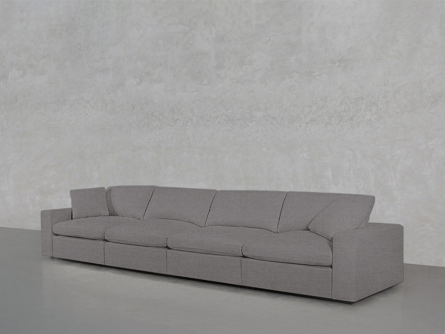 The 4-Seat Modular Sofa in light gray, featuring clean lines and square armrests, is set against a textured light gray wall on a smooth gray floor.