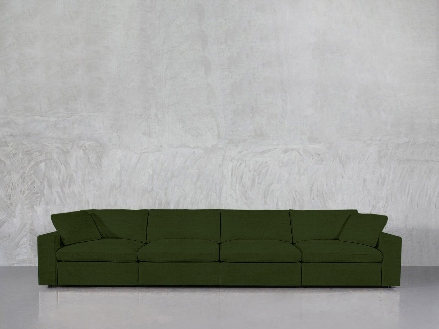 The 4-Seat Modular Sofa in modern dark green features four seat cushions and low, angled armrests, positioned against a textured light gray wall on a glossy floor.